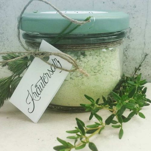 Grobes Kräutersalz in Glas mit frischem Thymian, Kräutersalz-Schrift und Grasdeko