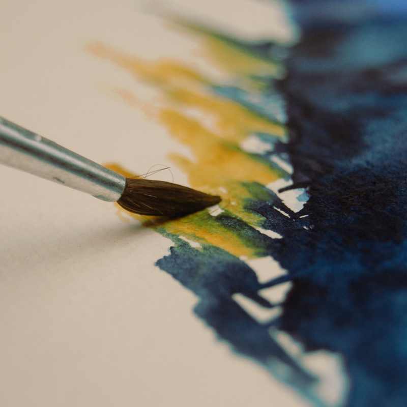 Vollbild Aquarellbild in Indigo und Ockergelb mit Aquarellpinsel, der gerade malt