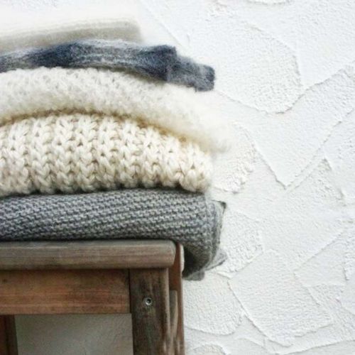 Ein Stapel handgestrickte Schals und Tücher in Naturfarben auf altem Hocker
