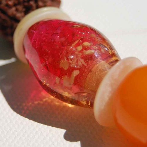 Eine große Glasolive in apricot-pink mit Einschlüssen schimmert in der Sonne