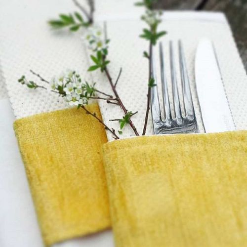 Naturfarbene Bestecktasche mit sonnengelber Banderole, Silberbesteck und Blütenzweig