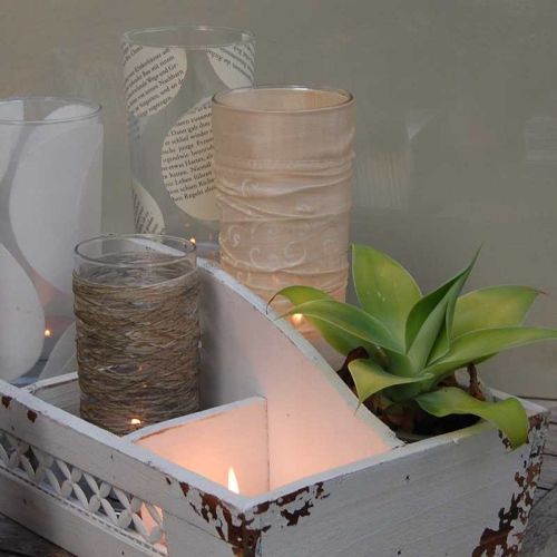 Verschiedene Glas-Windlichter mit Stoff- oder Papierhülle in Shabby-Holzkorb