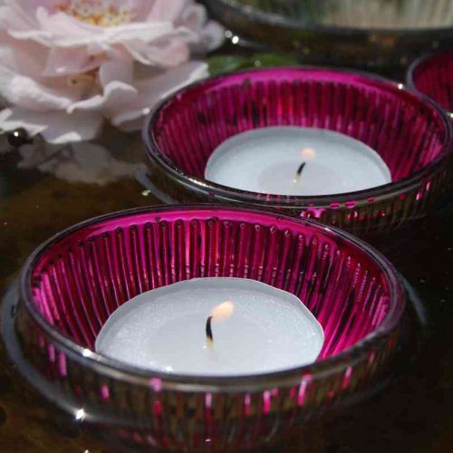 Pinkfarbene Glas-Schwimmschalen mit brennenden Teelichtern schwimmend